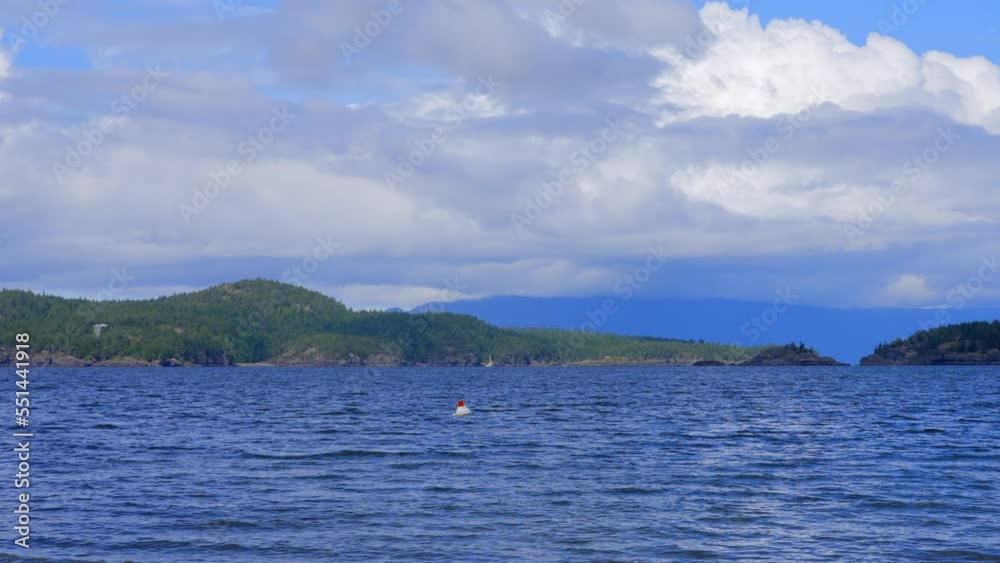 Establishing shot of ocean view with mountains, blue sky and white clouds in slow motion at summer day in Vancouver, Canada, North America. Day time on May 2022. Still camera. ProRes 422 HQ. Establishing shot of ocean view with mountains, blue sky and white clouds in slow motion at summer day in Vancouver, Canada, North America. Day time on May 2022. Still camera. ProRes 422 HQ.