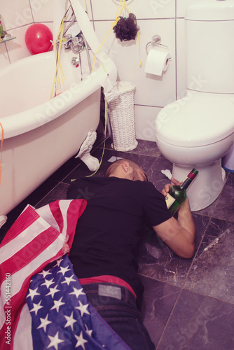Party, hangover and drunk man in bathroom sleeping after celebration, festival and house party in usa. After party, alcohol and male on floor by toilet of social event, new years eve and house party photo