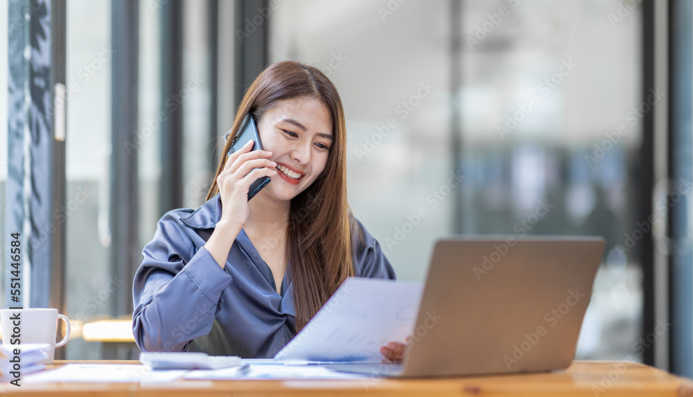 Asian Businesswoman Using laptop computer and working at office with calculator document on desk, doing planning analyzing the financial report, business plan investment, finance analysis concept.
