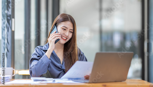 Asian Businesswoman Using laptop computer and working at office with calculator document on desk, doing planning analyzing the financial report, business plan investment, finance analysis concept. 