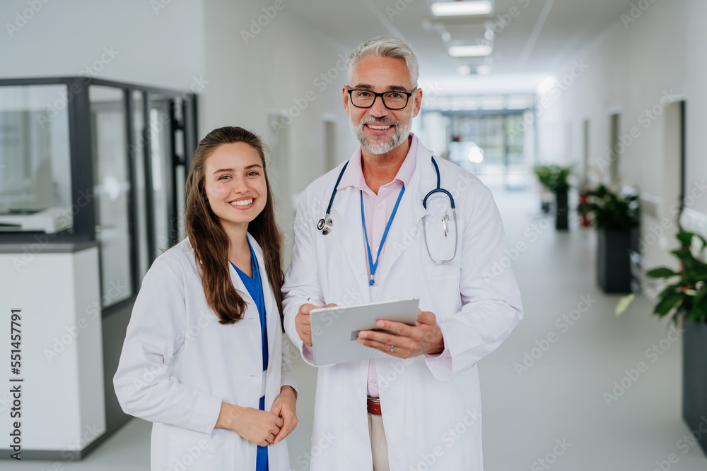 Portrait of elderly doctor with his younger colleague at hospital corridor. Health care concept. Portrait of elderly doctor with his younger colleague at hospital corridor. Health care concept.