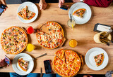 Hands taking pizza slices from wooden table