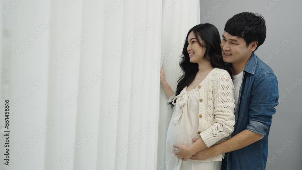 married couple is expecting baby. man embracing and talking with his pregnant wife while looking view through the window at home married couple is expecting baby. man embracing and talking with his pregnant wife while looking view through the window at home
