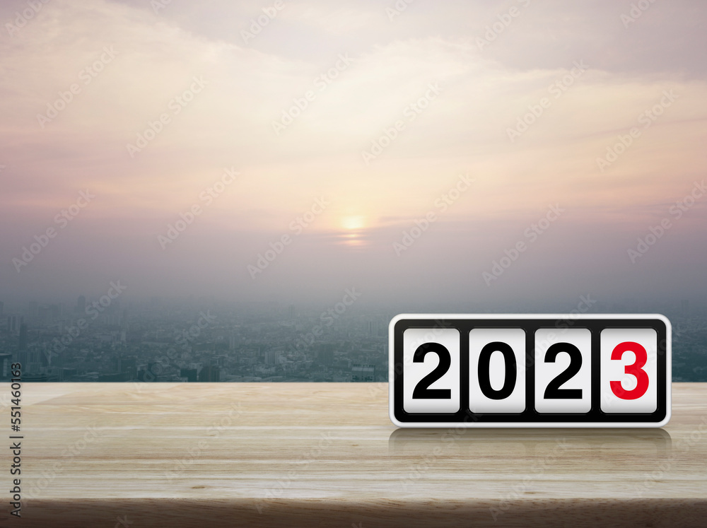 Retro flip clock with 2023 text on wooden table over modern city tower and skyscraper at sunset, vintage style, Happy new year 2023 cover concept