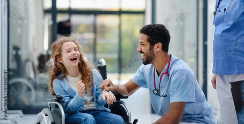 Young multiracial doctor having fun with little girl on wheelchair.