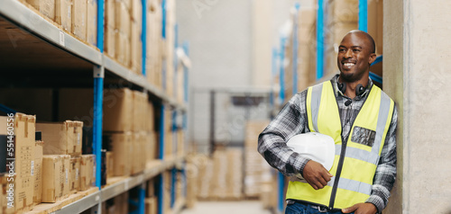 Happy warehouse picker looking away with a smile, man stands in a logistics centre with a voice picking headset and a helmet photo