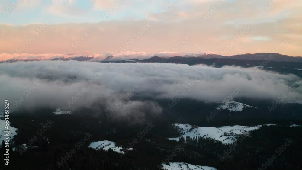 Drone flight among beautiful low clouds and mists creeping over the snow-covered mountain slopes, the Rhodopes in Bulgaria at winter sunrise. Drone flight among beautiful low clouds and mists creeping over the snow-covered mountain slopes, the Rhodopes in Bulgaria at winter sunrise.
