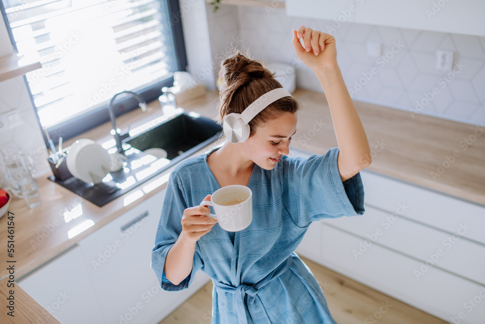 Young woman listening music and enjoying cup of coffee at morning, in her kitchen. - obrazy, fototapety, plakaty 