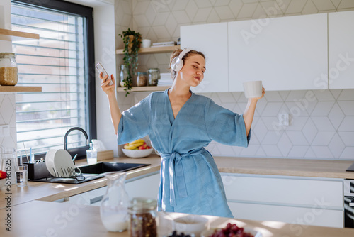 Young woman listening music and enjoying cup of coffee at morning, in her kitchen.