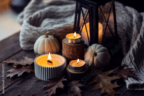 Cozy autumn composition with aromatic candle, pumpkins, wool sweater, leaves, cinnamon. Aromatherapy on a grey fall morning, home atmosphere of cosiness and relax. Wooden background close up.