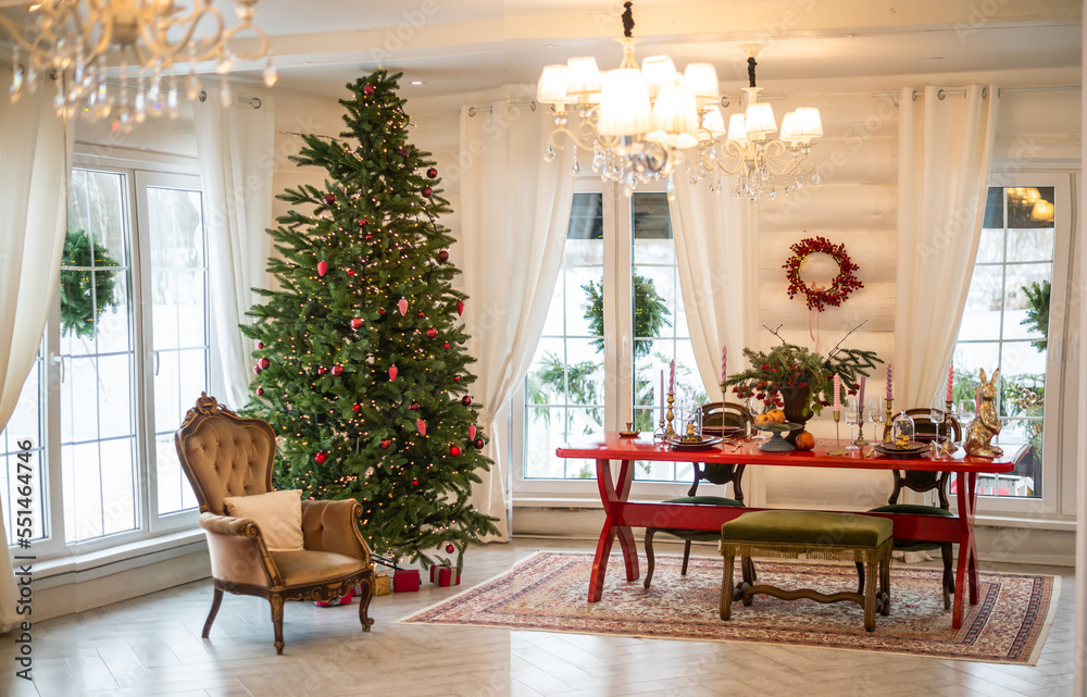room decorated for Christmas. A red table with candles and a Christmas tree. White beautiful house with large windows