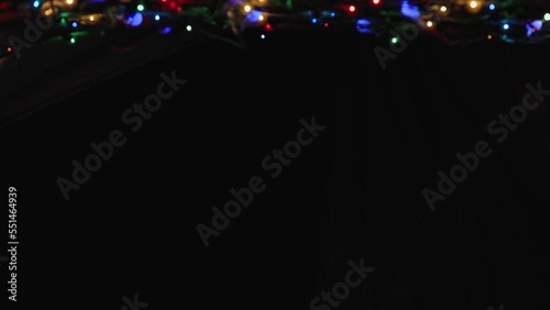 Glowing Christmas garland at the top of the frame on a black background. Place to copy. New Year multi-colored lights in defocus. Beautiful holiday card, video for intro, text, intro. UHD 4K.