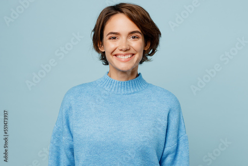 Young cheerful joyful satisfied smiling happy friendly caucasian woman in knitted sweater looking camera isolated on plain pastel light blue cyan background studio portrait. People lifestyle concept