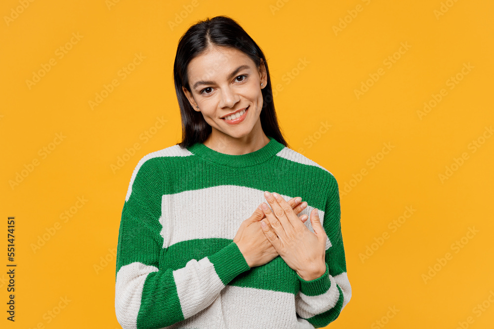 Young thankful grateful smiling fun brunette latin woman wear casual cozy green knitted sweater put folded hands on heart isolated on plain yellow background studio portrait People lifestyle concept. Young thankful grateful smiling fun brunette latin woman wear casual cozy green knitted sweater put folded hands on heart isolated on plain yellow background studio portrait People lifestyle concept.