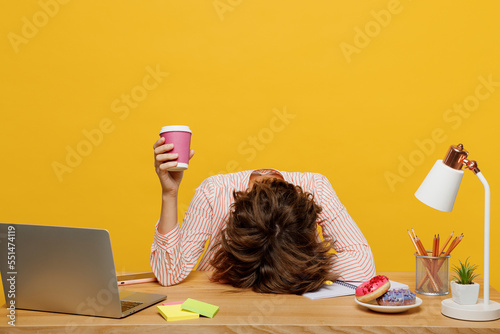 Young employee business woman wear shirt sit work at office desk with laptop hold takeaway paper cup coffee to go put head on desk isolated on plain yellow color background Achievement career concept