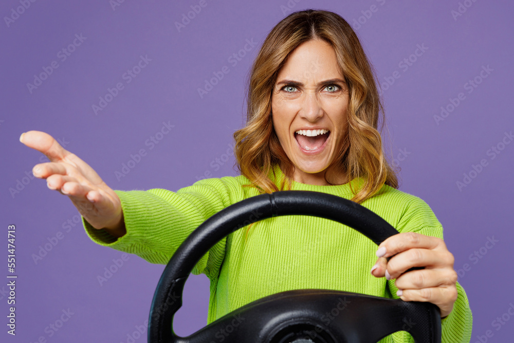 Young sad angry mad woman 30s wearing casual green knitted sweater holding steering wheel driving car spread hands isolated on plain pastel purple background studio portrait. People lifestyle concept. Young sad angry mad woman 30s wearing casual green knitted sweater holding steering wheel driving car spread hands isolated on plain pastel purple background studio portrait. People lifestyle concept.