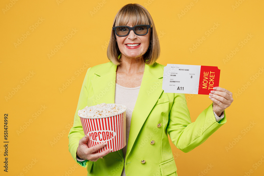 Elderly happy smiling cheerful fun cool woman 50s years old in 3d glasses watch movie film hold ticket bucket of popcorn cup of soda pop in cinema isolated on plain yellow background studio portrait. Elderly happy smiling cheerful fun cool woman 50s years old in 3d glasses watch movie film hold ticket bucket of popcorn cup of soda pop in cinema isolated on plain yellow background studio portrait.