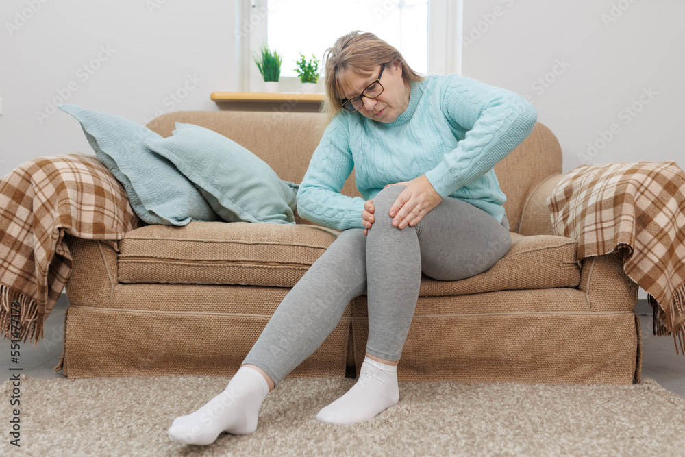 Mature woman suffering from knee ache on sofa Mature woman suffering from knee ache on sofa