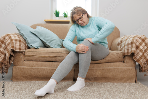 Mature woman suffering from knee ache on sofa