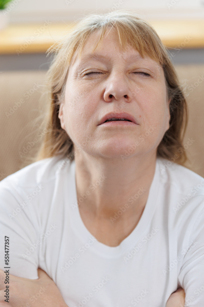 Indoor portrait of happy elderly woman hugging herself, giving support, showing self-respect and love, sitting on couch with closed eyes in white t-shirt. Human emotions, body language Indoor portrait of happy elderly woman hugging herself, giving support, showing self-respect and love, sitting on couch with closed eyes in white t-shirt. Human emotions, body language