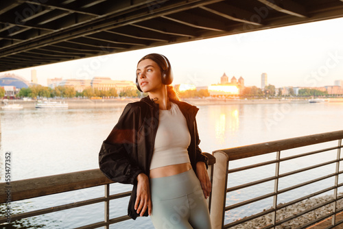Young woman listening to music with headphones walking along river bank