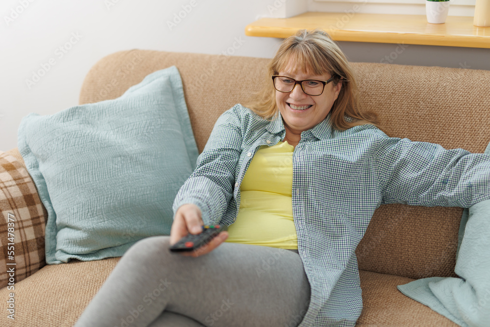 Obraz premium Mature blond woman watching television on sofa, in living room.
