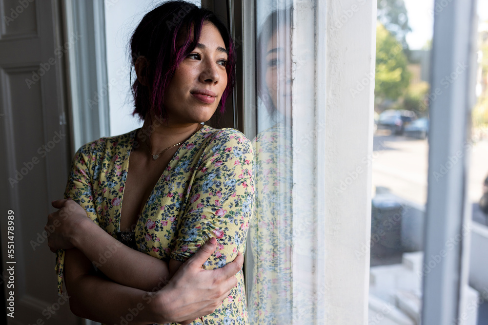Smiling young woman looking through window at home Smiling young woman looking through window at home