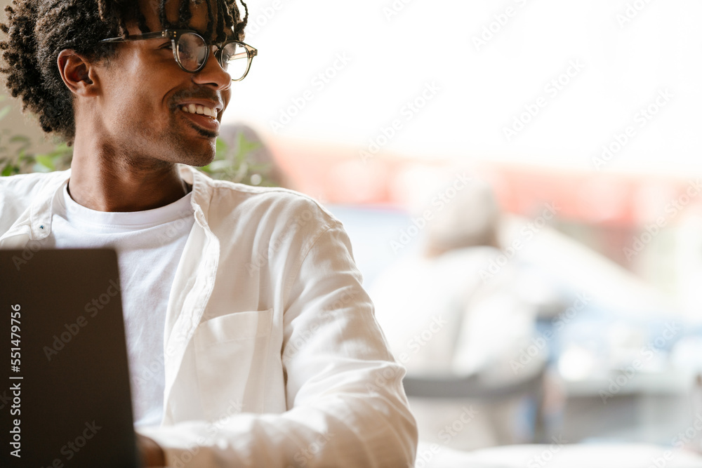 Obraz premium Young african american man smiling and using laptop in cafe indoors