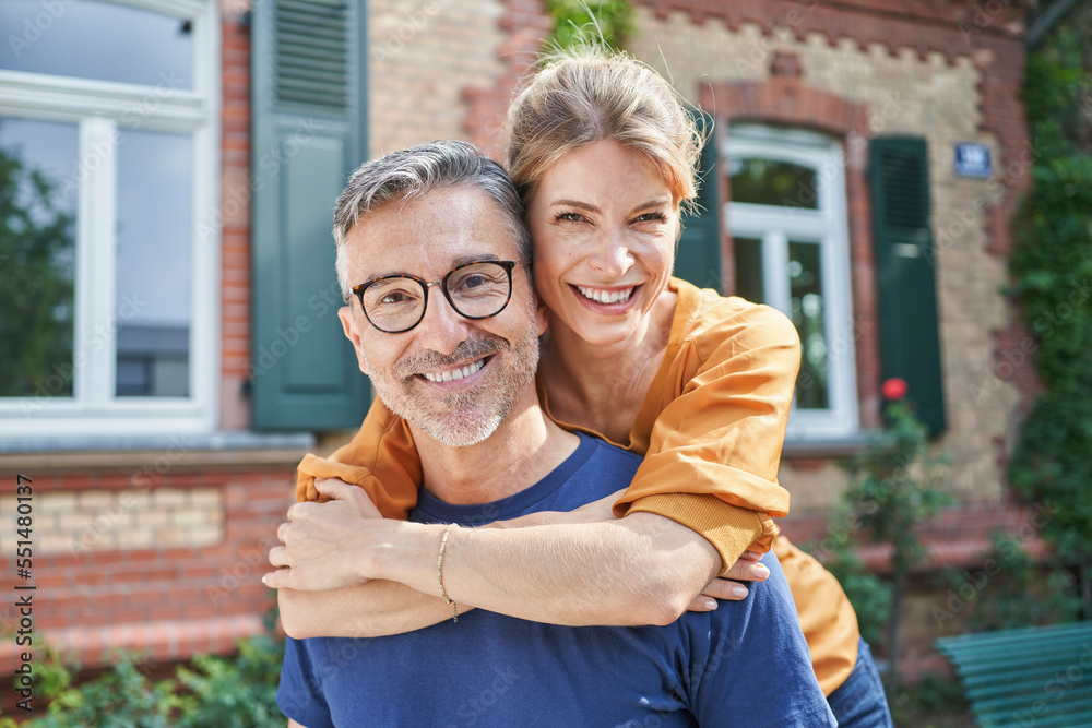 Happy woman embracing mature man from behind in front of house Happy woman embracing mature man from behind in front of house