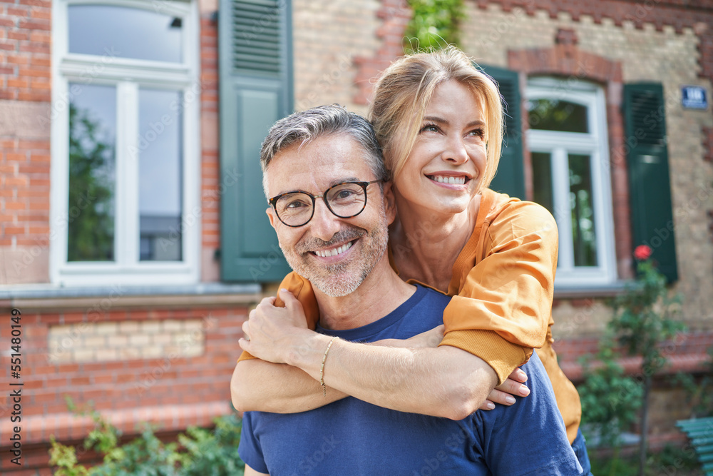 Happy woman embracing man from behind in front of house Happy woman embracing man from behind in front of house