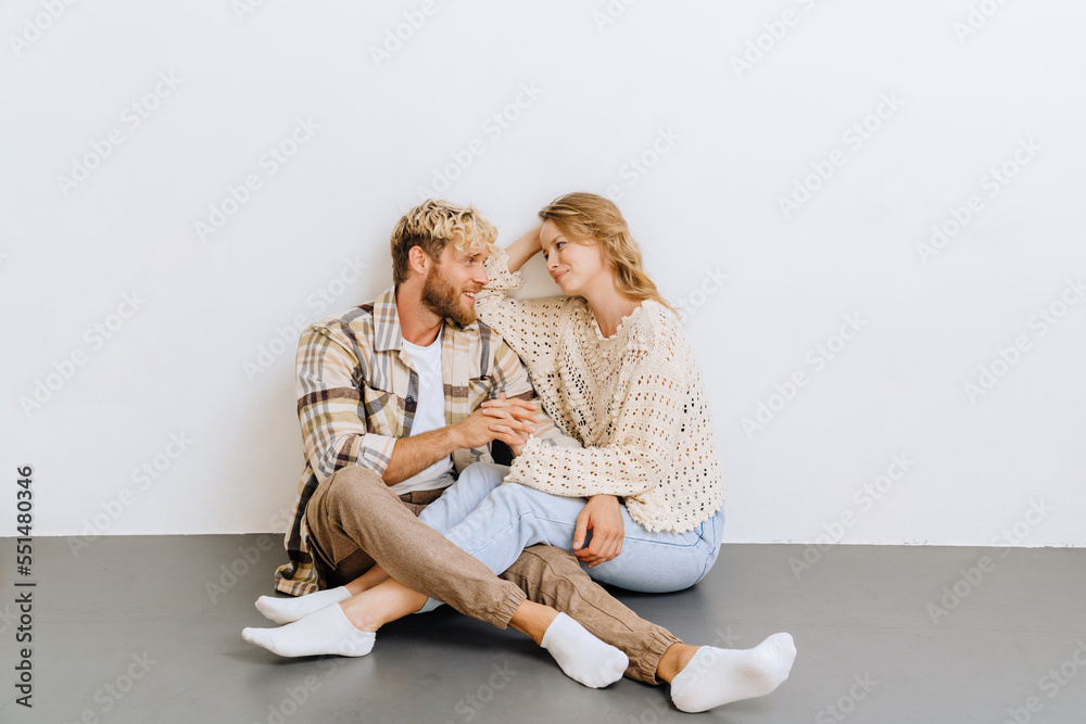 Young joyful couple holding hands while sitting on the floor isolated Young joyful couple holding hands while sitting on the floor isolated