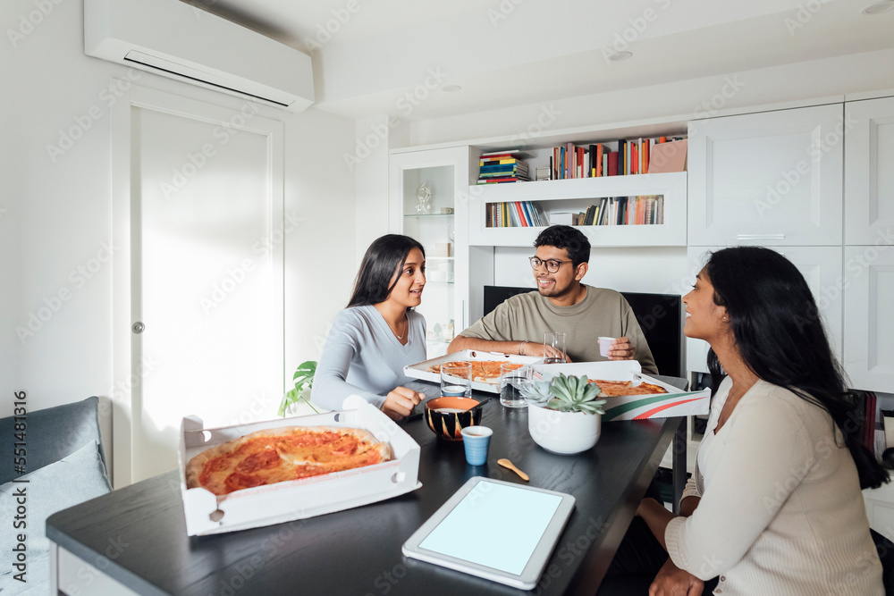 Happy women and man discussing and having pizza at dining table in living room Happy women and man discussing and having pizza at dining table in living room