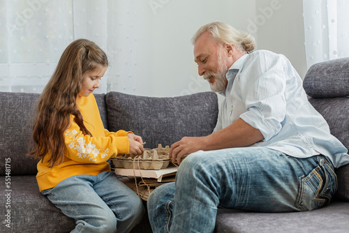 Grandfather and granddaughter bunching waste paper together on sofa photo