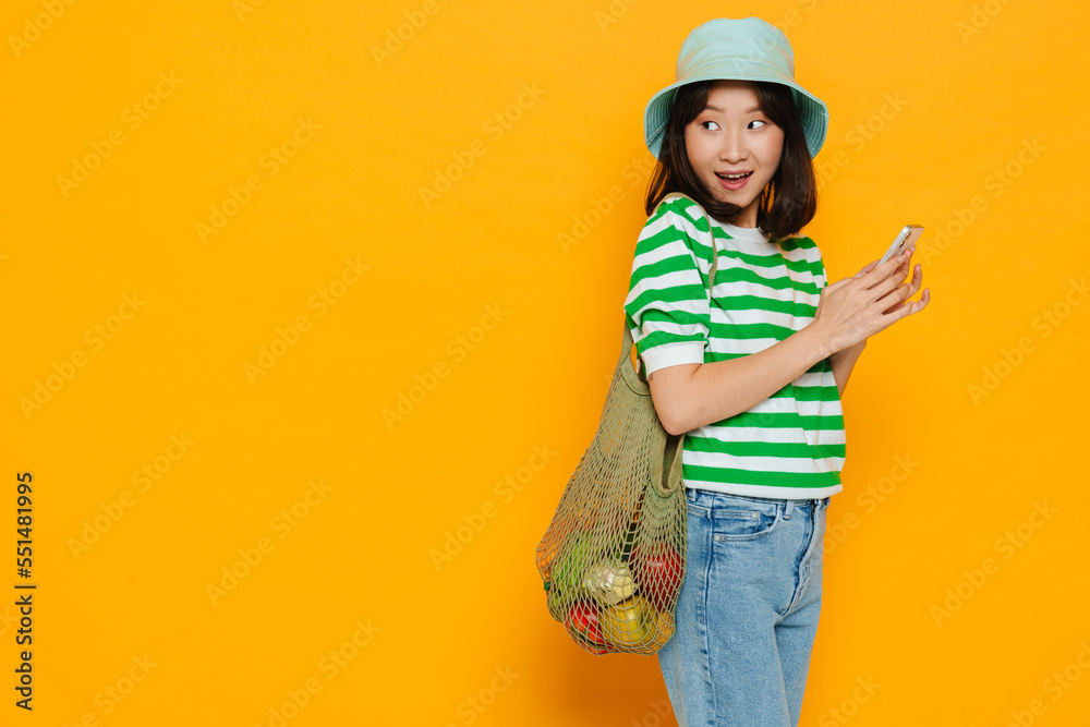 Asian girl with string bag of vegetables using mobile phone isolated