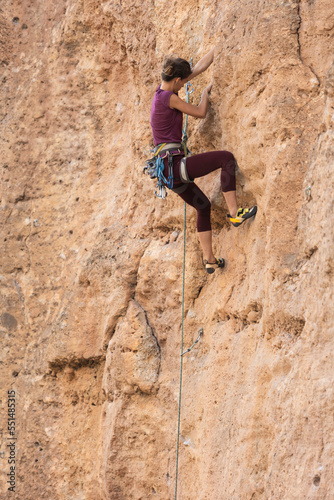 The girl climbs the rock. The climber is training to climb the rock. A strong athlete overcomes a difficult climbing route. Extreme hobby. A woman goes in for sports in nature.