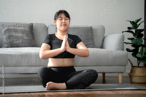 Asian chubby woman sitting on the floor in living room practice yoga lesson. female having meditate training class.