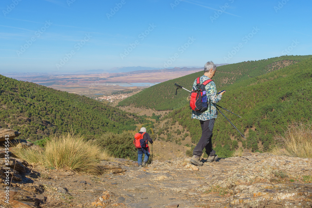 A woman using her cell phone while enjoying her walk in the mountains, accompanied by a male friend.