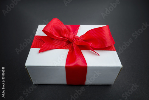 Gift box with a red ribbon on a black surface.