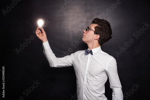 Young nerd guy with bulb standing against black background