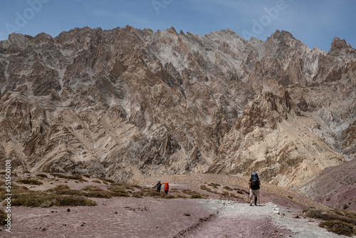 mountain trekkers walking with backpacks through the Himalayas. Raw mountain landscape with people in the background.