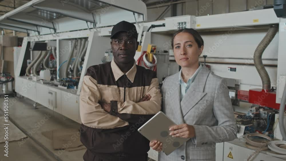 Waist up portrait shot of Caucasian female manager with tablet and African American worker posing together for camera at furniture factory Waist up portrait shot of Caucasian female manager with tablet and African American worker posing together for camera at furniture factory
