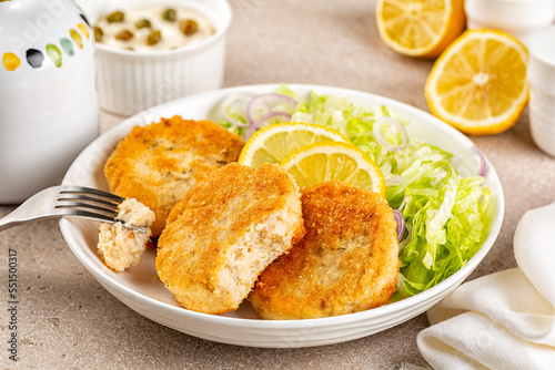 Eating Fish cakes or burger, or putties. Made from ground perch and tuna with herbs, breaded and fried, served with iceberg salad, lemon slices.