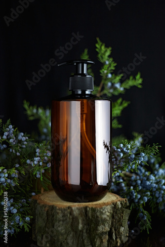 A brown plastic jar with a pipette on the background of pine needles with blue berries. Container for cosmetics on the background of plants.