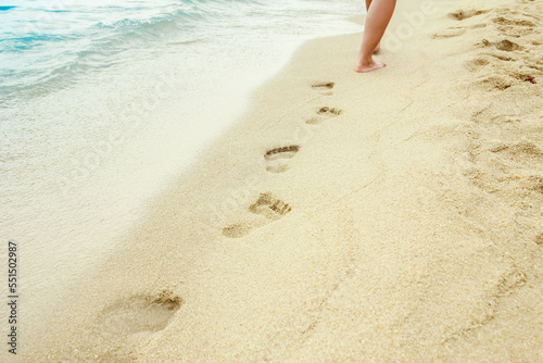 A Beach travel - woman relaxing walking on a sandy beach leaving footprints in the sand. Close up detail of female feet on golden sand at a beach in Greece. Background.