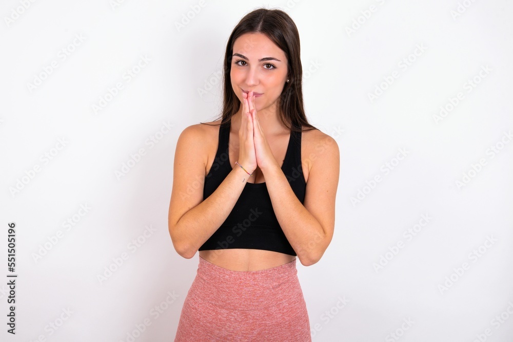 Fototapeta premium Young caucasian woman wearing sportswear over white background keeps palms pressed together in front of her having regretful look, asking for forgiveness. Forgive me please.