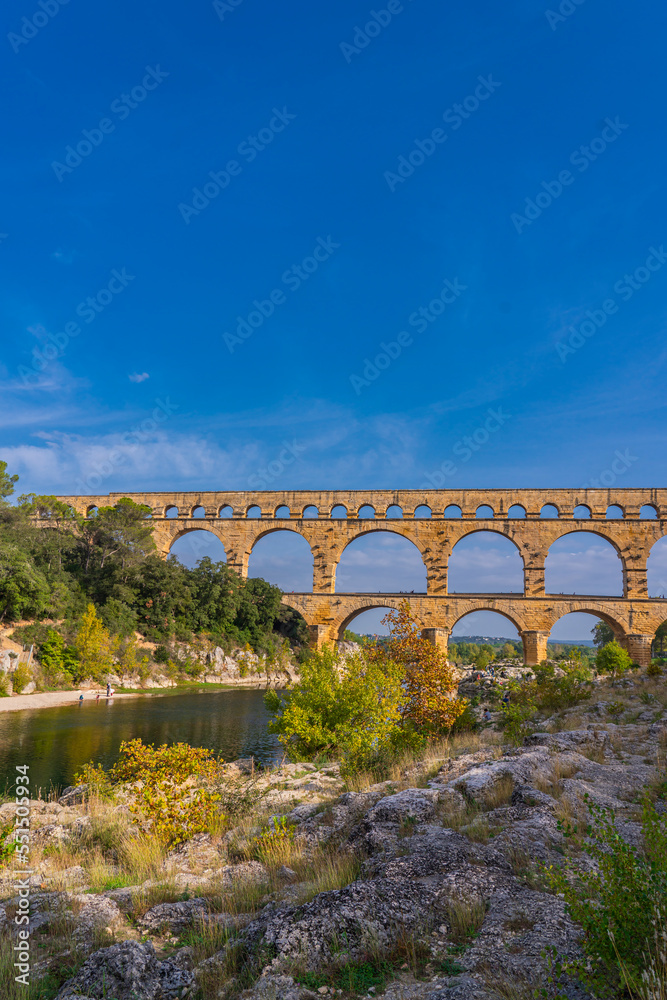 Vertical view to the orange limestone Pont du Gard three-tiered aqueduct at the river Gardon.