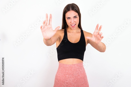 Dissatisfied Young caucasian woman wearing sportswear over white background frowns face, has disgusting expression, shows tongue, expresses non compliance, irritated with somebody.