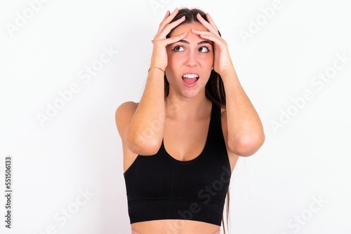 Horrible, stress, shock. Portrait emotional crazy Young caucasian woman wearing sportswear over white background clasping head in hands. Emotions, facial expression concept.