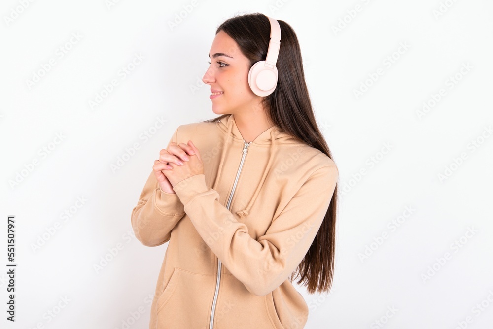 Young caucasian woman wearing sweatshirt over white background wears stereo headphones listening to music concentrated and looking aside with interest. Young caucasian woman wearing sweatshirt over white background wears stereo headphones listening to music concentrated and looking aside with interest.