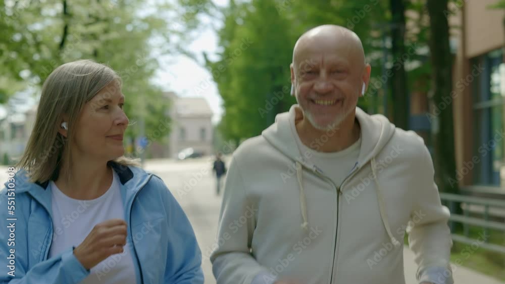 Matured smiled couple running on the street wearing earphones and listen to music while training. Sport, relationship and healthy lifestyle concept Matured smiled couple running on the street wearing earphones and listen to music while training. Sport, relationship and healthy lifestyle concept